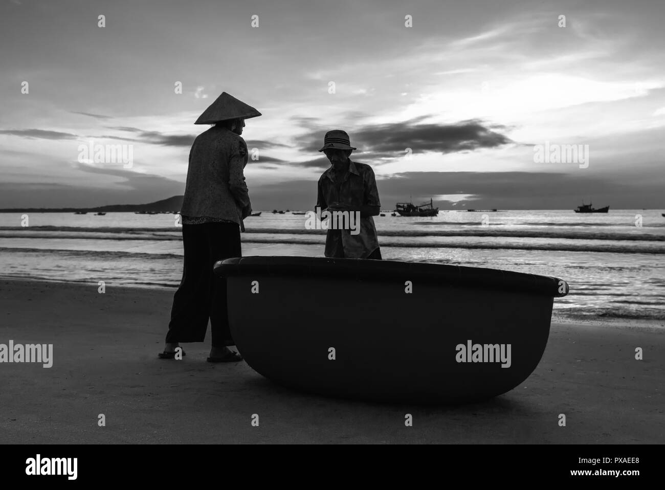 La pareja de ancianos en una hermosa playa al amanecer junto a una canasta barco mirando para la captura de los pescadores en la orilla esperando una buena cosecha Foto de stock