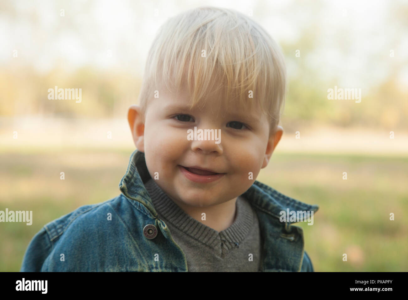 Blanco 1 año viejo muchacho rubio posando y mirando a una cámara de gran campo abierto de hierba con un colorido en otoño el clima. Clima: soleado y seco. Foto de stock