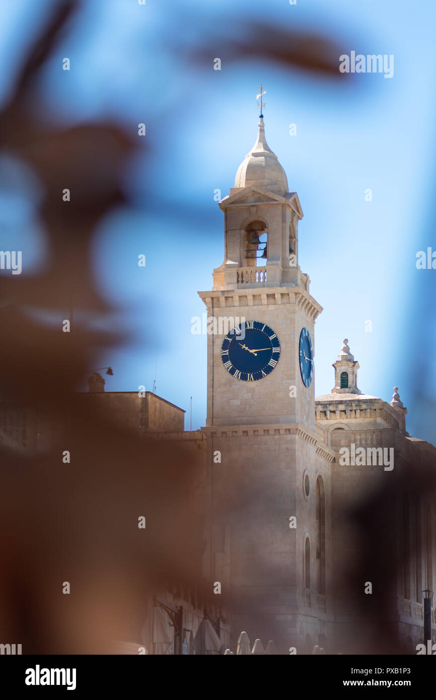 Iglesia de San Lorenzo, reloj de Birgu, Vittoriosa, Malta entre plantas. Espacio para el texto. Vertical. Vista lateral. Foto de stock
