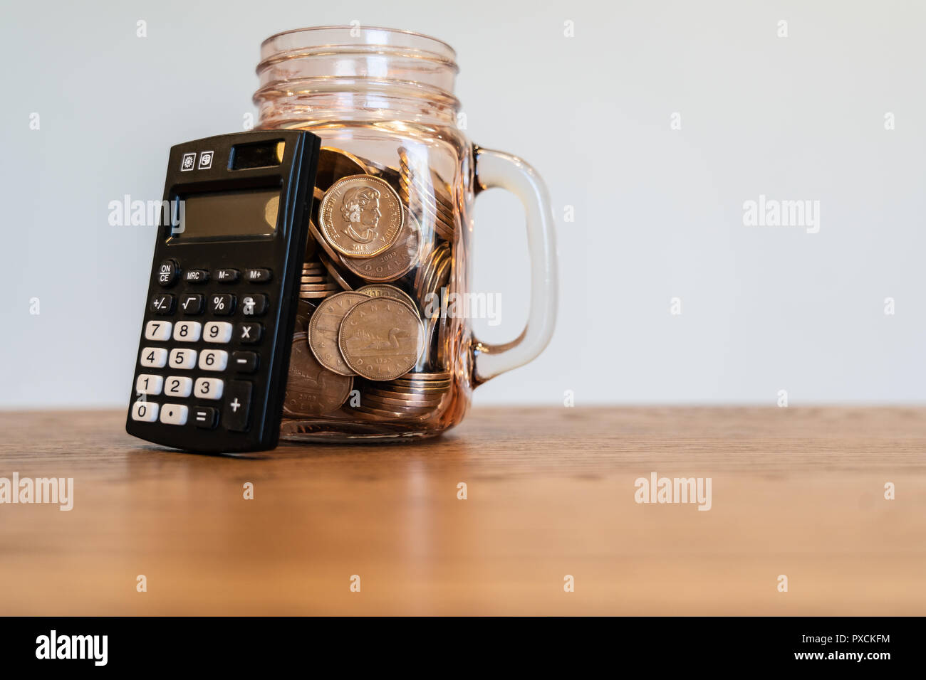 Calculadora de bolsillo junto a jarra llena de monedas para mostrar el  ahorro Fotografía de stock - Alamy