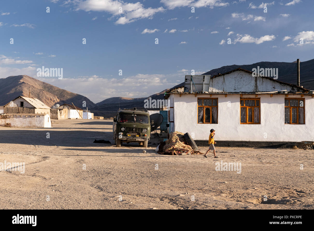 Chico local camina por una casa encaladas en la noche en la aldea, Bulunkul Bulunkul, el Pamir Highway, Gorno Badakhshan, Tayikistán Foto de stock
