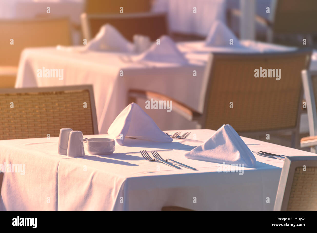 Sillas y mesas al atardecer en el restaurante del hotel. Cubertería y napkings en tablas. Foto de stock
