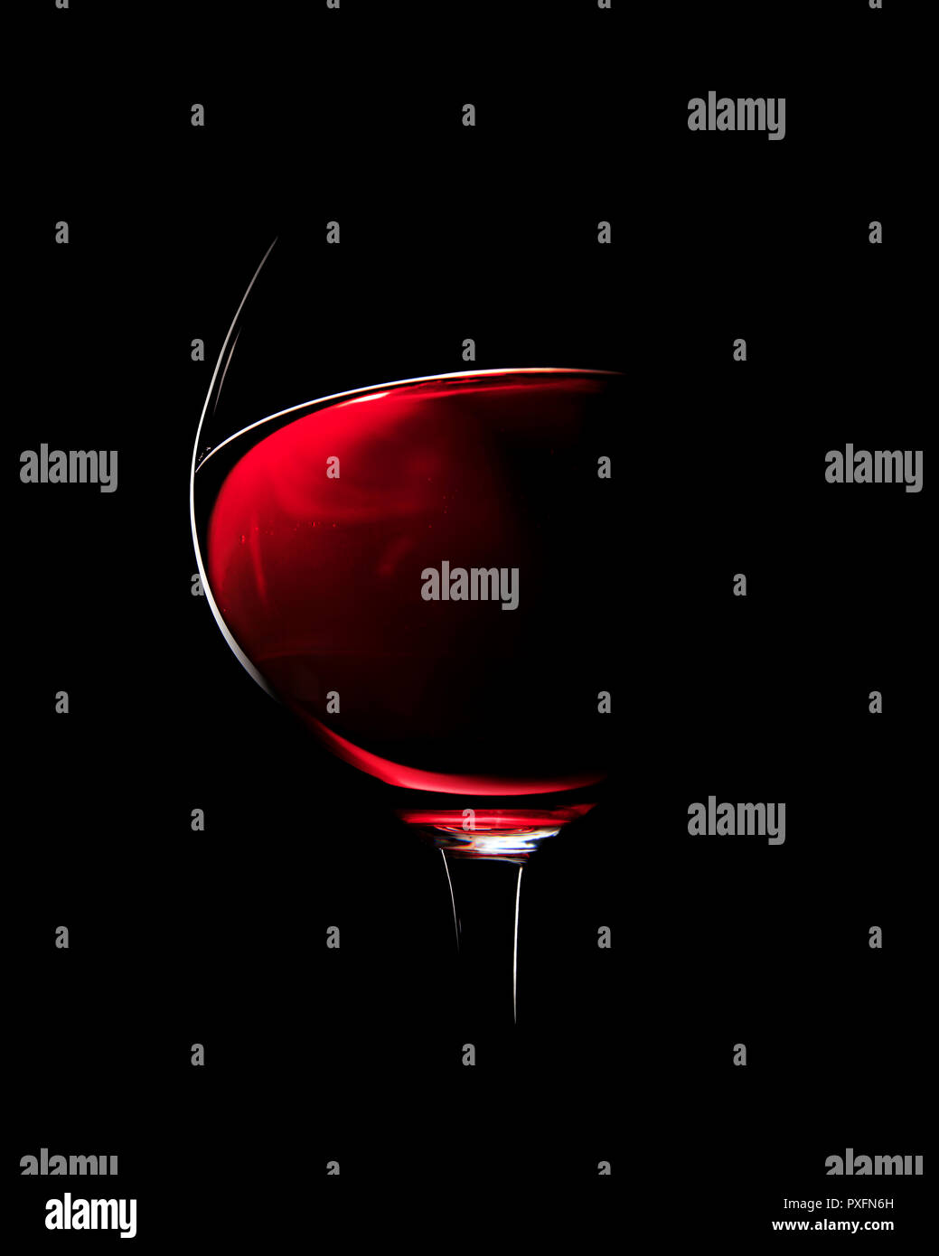 Un vaso de vino tinto fotografiado con luz rim contra el fondo negro (enfoque en el borde del cristal) Foto de stock