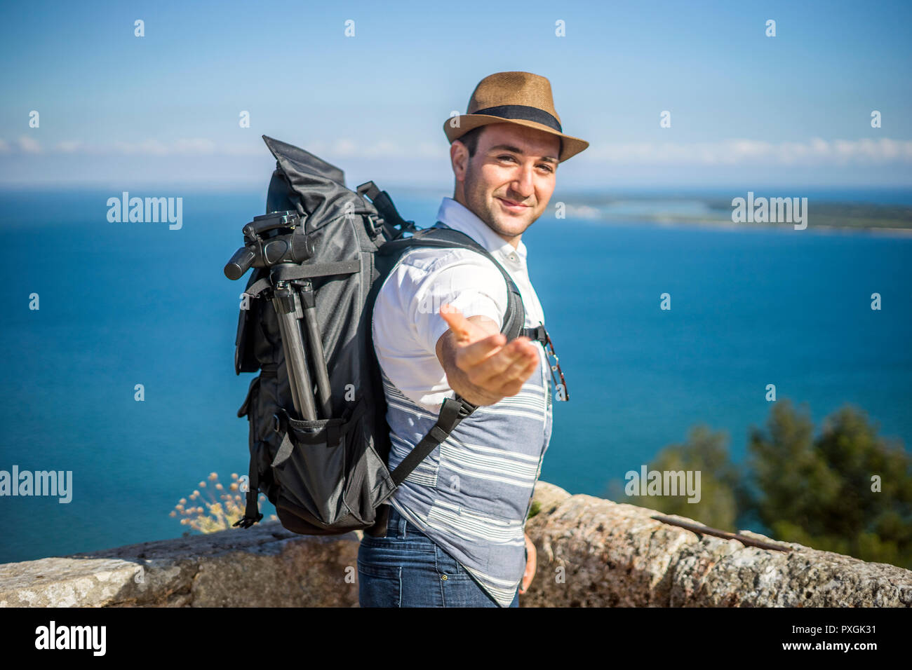 Feliz viajero con mochila grande disfrutando del mar, invitando a que se unan a él Foto de stock