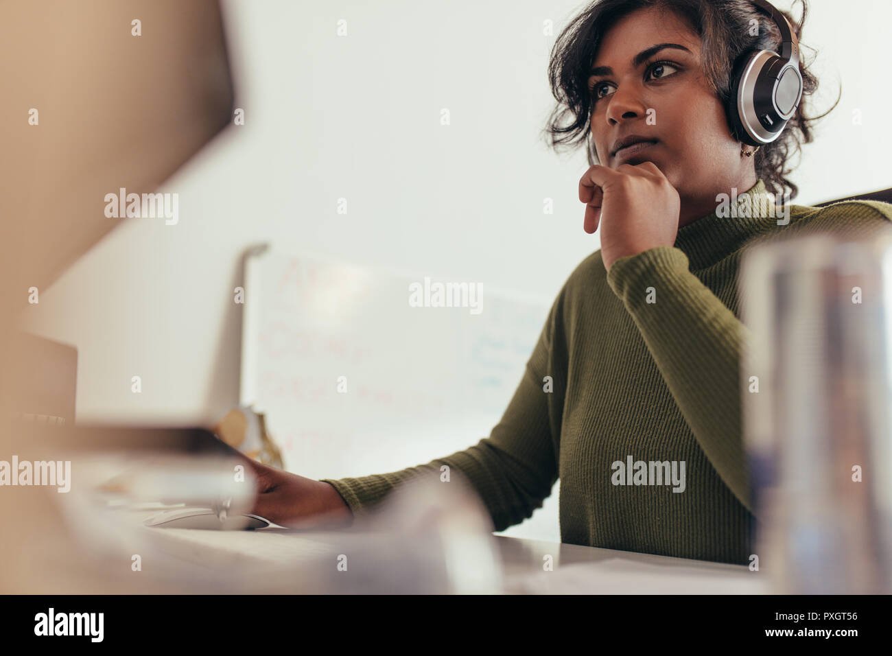 Retrato de mujer vistiendo auriculares mirando al monitor del ordenador. Equipo Femenino programador que trabaja en su oficina. Foto de stock