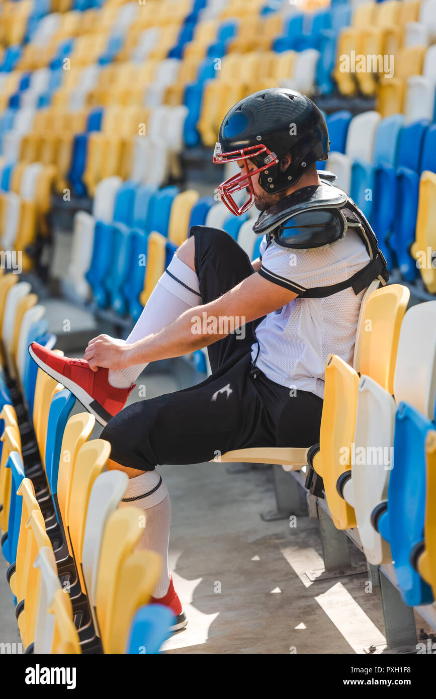 Vista lateral del joven jugador de fútbol americano sentado en tribunas en  el estadio deportivo y zapatillas de costura Fotografía de stock - Alamy