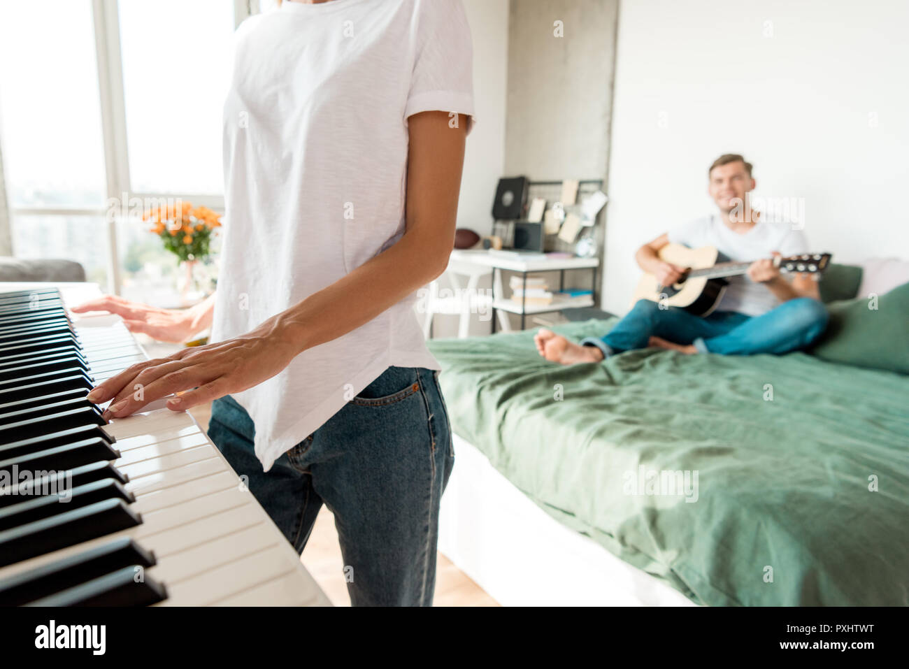 Vista parcial del hombre tocando la guitarra acústica en la cama mientras  novia jugando electronic piano en casa Fotografía de stock - Alamy