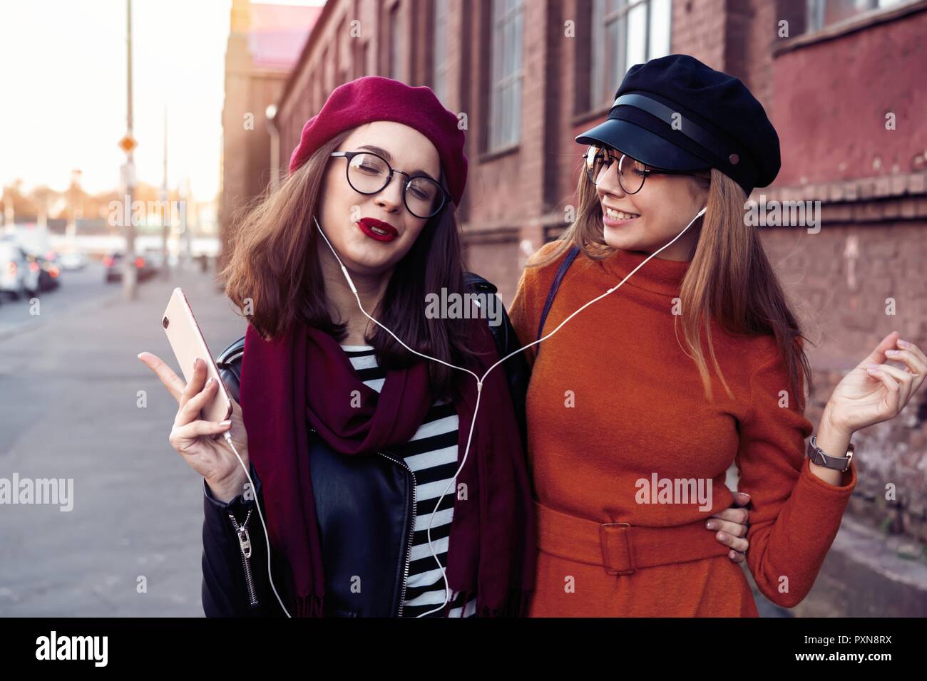 Dos alegres chicas bailando mientras escucha música en el smartphone, la ciudad al aire libre. Foto de stock