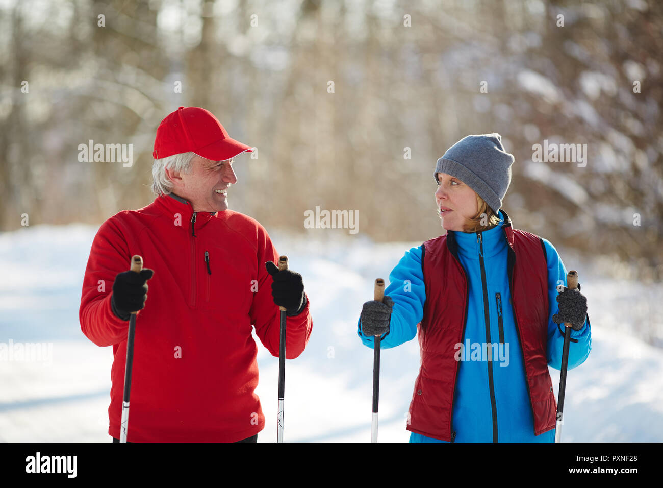 Dos personas maduras en activewear mirando el uno al otro, mientras que en invierno se puede esquiar bosque Foto de stock