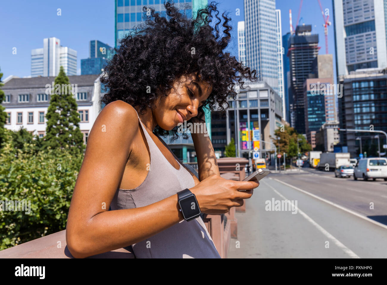 Alemania, Frankfurt, retrato de mujer sonriente con el pelo rizado usando un teléfono celular en la ciudad Foto de stock