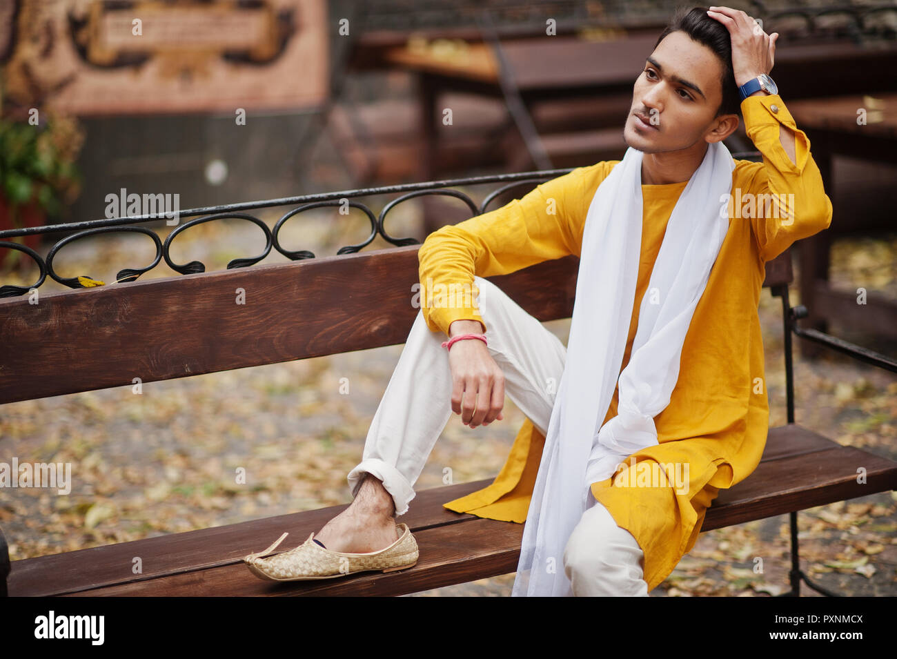 India hombre elegante en amarillo con tradicional pañuelo blanco plantea banco exterior Fotografía de stock -