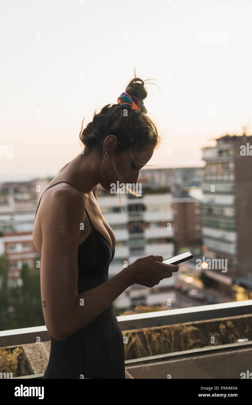 Joven mujer vistiendo vestido negro con teléfono celular en balcón Foto de stock