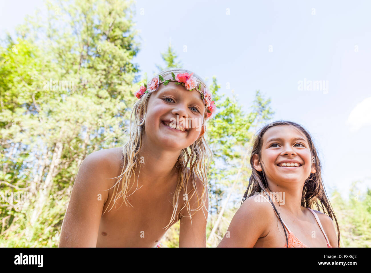Retrato de niña alegre portando corona de flores y amigo al aire libre en verano Foto de stock