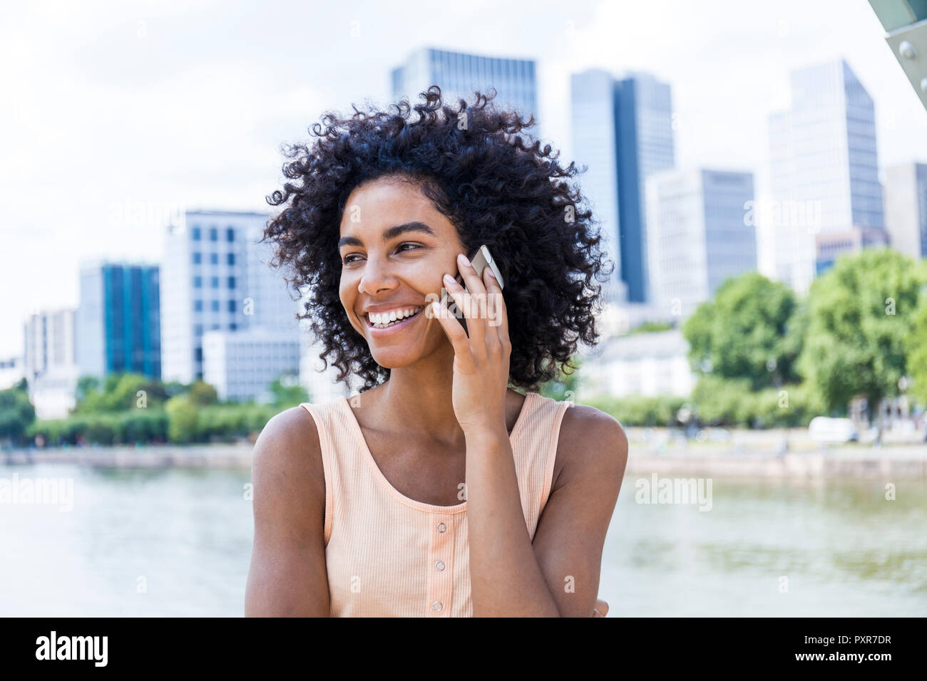 Alemania, Frankfurt, retrato de mujer sonriente con el pelo rizado en el teléfono Foto de stock