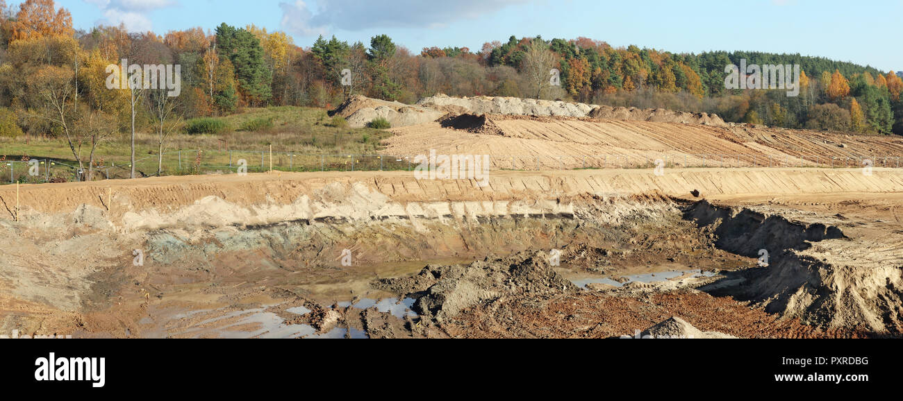 Un gran hills y fosos de arena y restos de una topadora pesada y tractores en un bosque de otoño sitio en construcción. Collage panorámica desde varios fuera Foto de stock