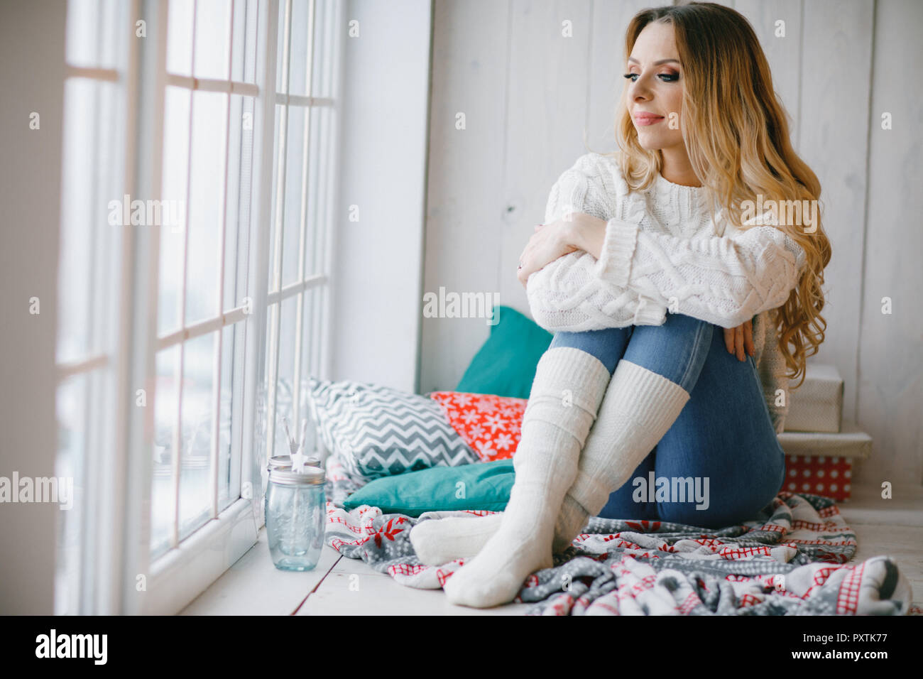 Mujer hermosa con el pelo rizado está sentado en la ventana aún en un  suéter de tejido y calentadores de pierna Fotografía de stock - Alamy