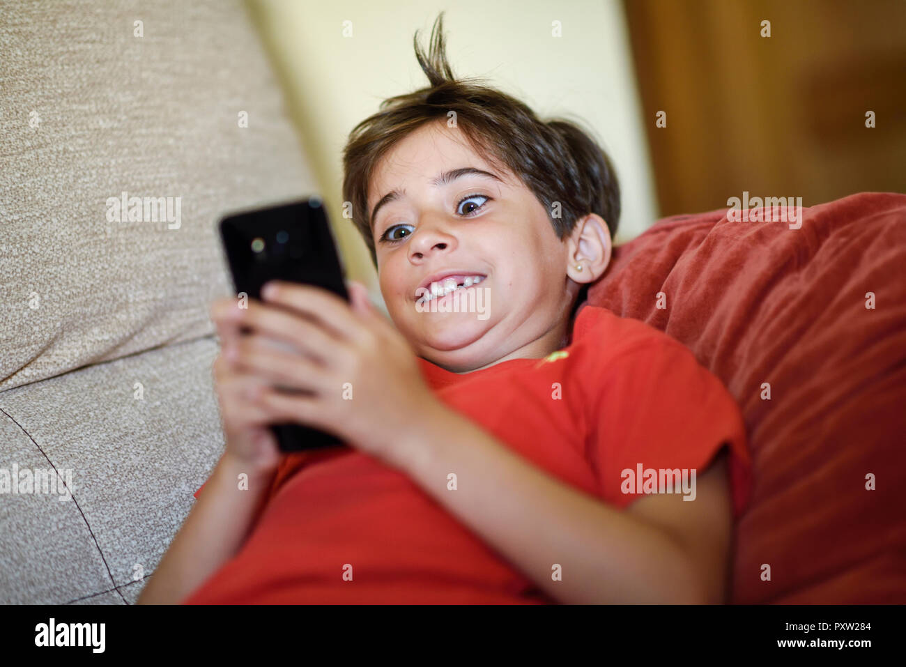 Retrato de niña acostada sobre el sofá starring en teléfono celular Foto de stock