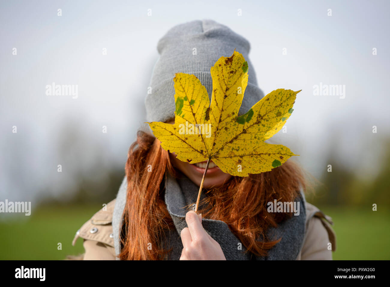 Adolescente escondiéndose detrás de hoja de otoño Foto de stock