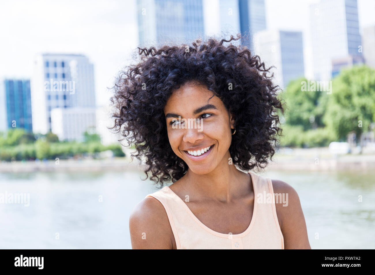 Alemania, Frankfurt, retrato de mujer sonriente con el pelo rizado en frente del río principal Foto de stock