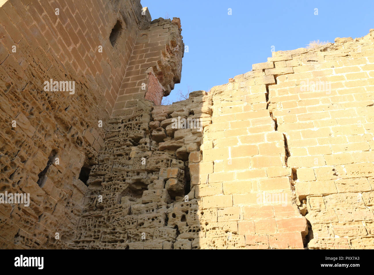 Grietas en las paredes erosionadas amarillo de la abandonada Montearagon castillo en la región de Aragón, España, contra un cielo azul profundo durante un día de verano Foto de stock