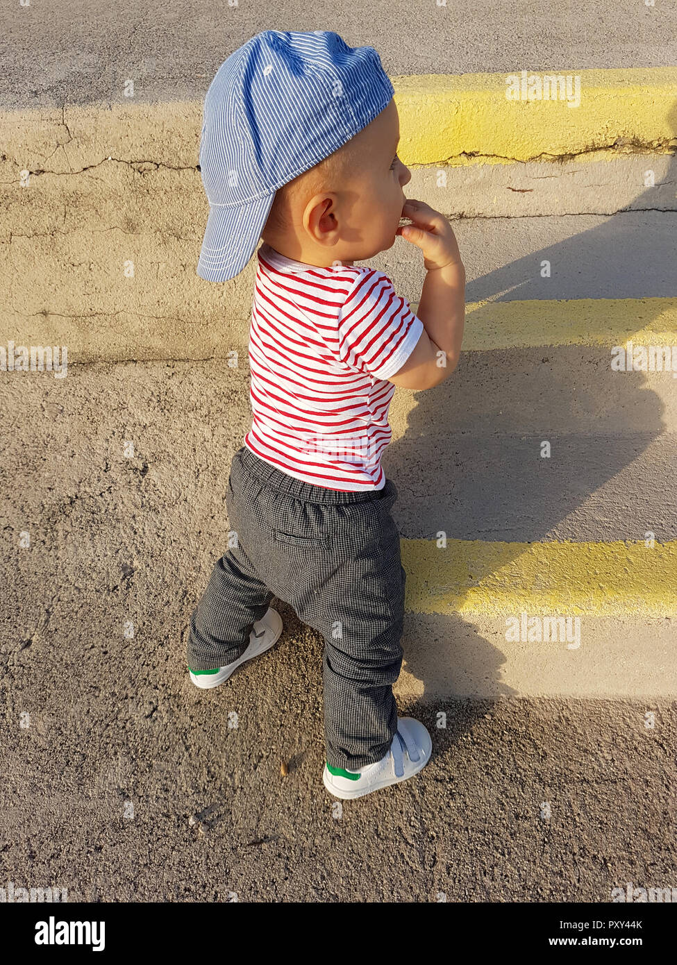 Cute Baby Boy 1 año llevaba una gorra hacia atrás y ropa rayas, cerca de retrato, bebé de pie sobre las escaleras Fotografía de stock - Alamy