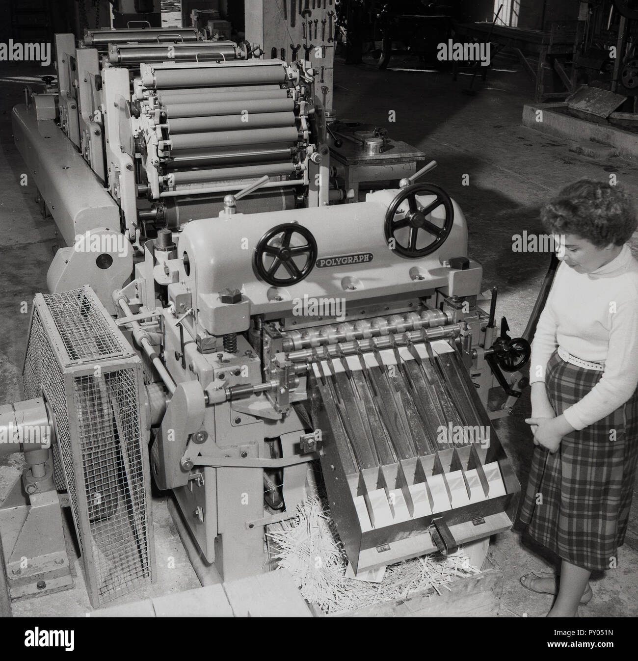 1950, histórico, una trabajadora de pie por una gran máquina de impresión larga, mostrando el amplio número de rotación de los rodillos de tinta utilizada en el proceso de impresión. Foto de stock