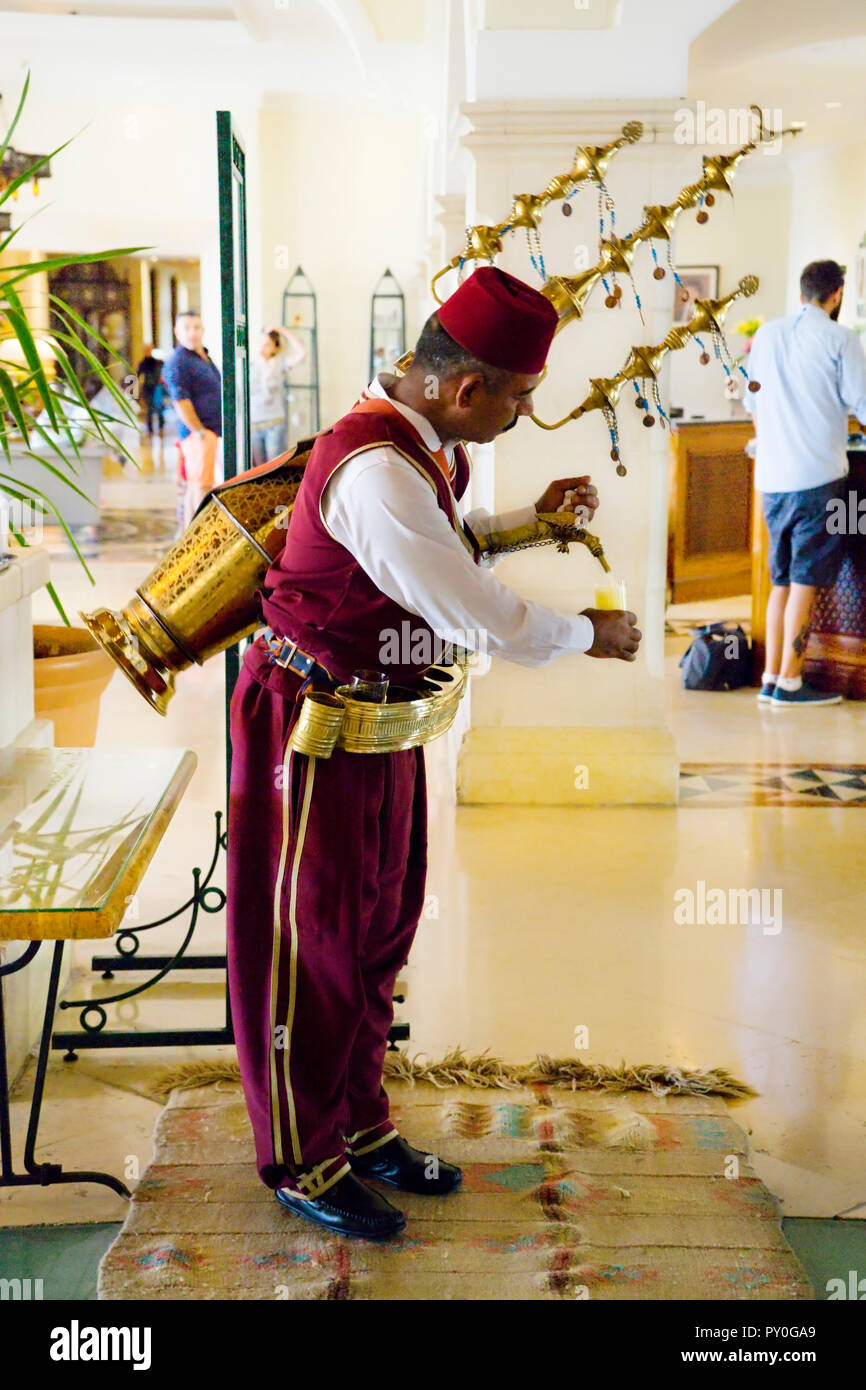 Un hombre árabe, vestida con ropa de estilo tradicional otomano, vierte zumo de frutas de una gran cobre, adornada, spouted receptáculo en la espalda, en el vestíbulo de un hotel, la Gobernación de Madaba, Jordania Foto de stock