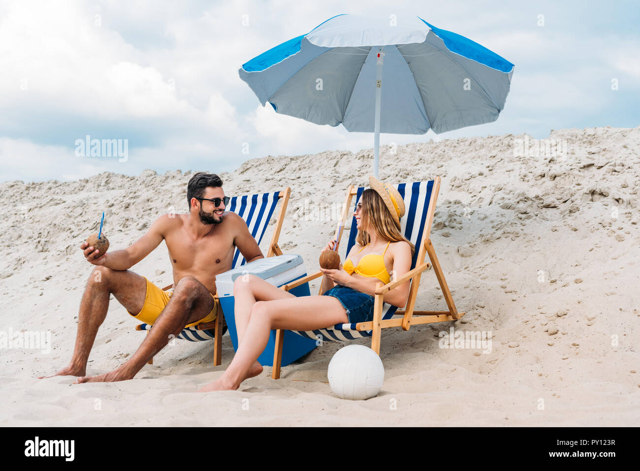 Hermosa pareja joven con cócteles de coco relajarse en reposeras en la  playa de arena Fotografía de stock - Alamy