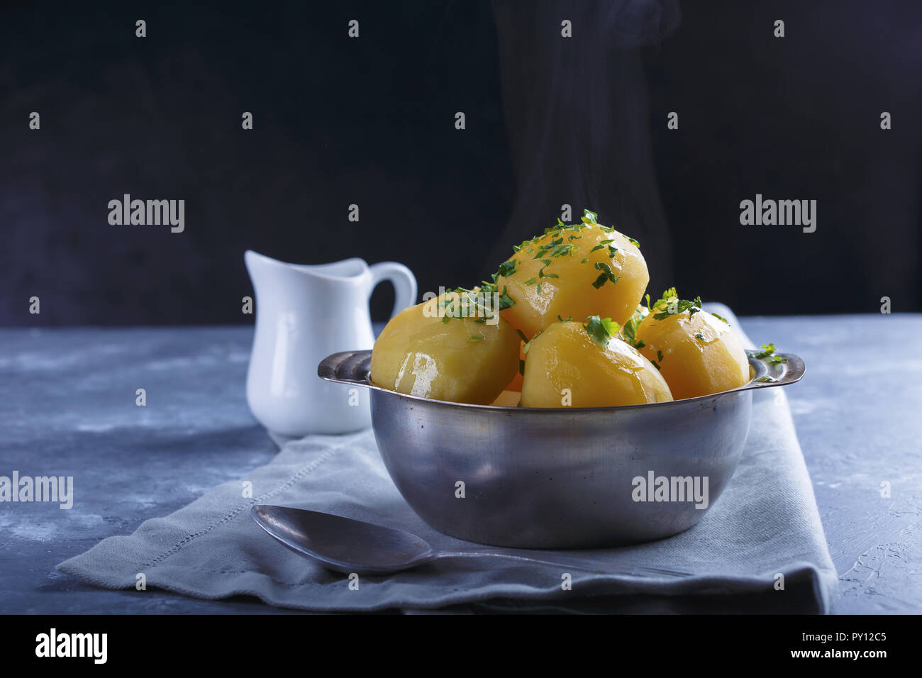 Patatas hervidas en caliente en una placa espolvoreada con verdes y humo sobre un fondo gris. Foto de stock