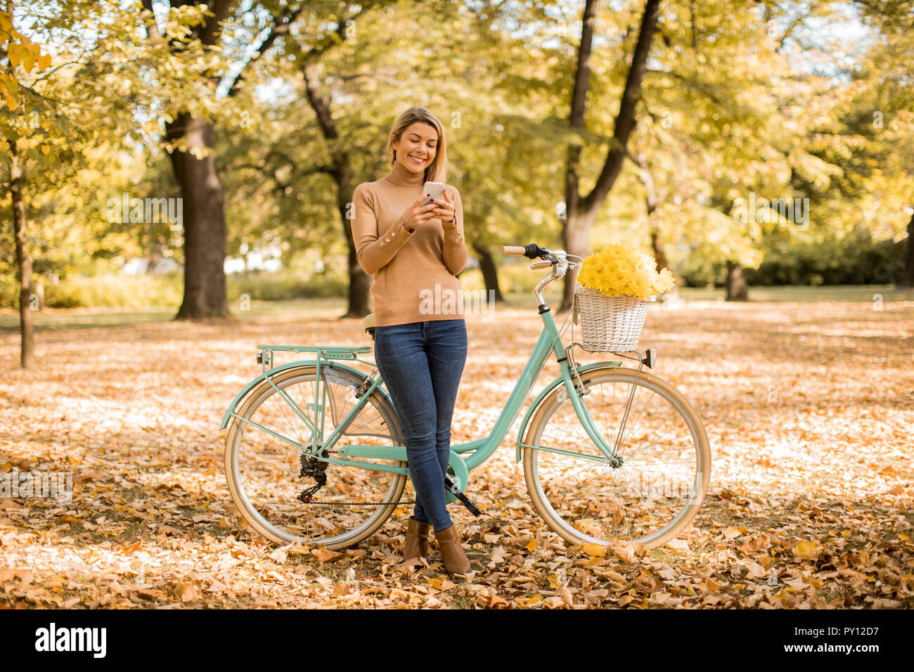 Cheerfull joven con bicicleta con smartphone en otoño park Foto de stock