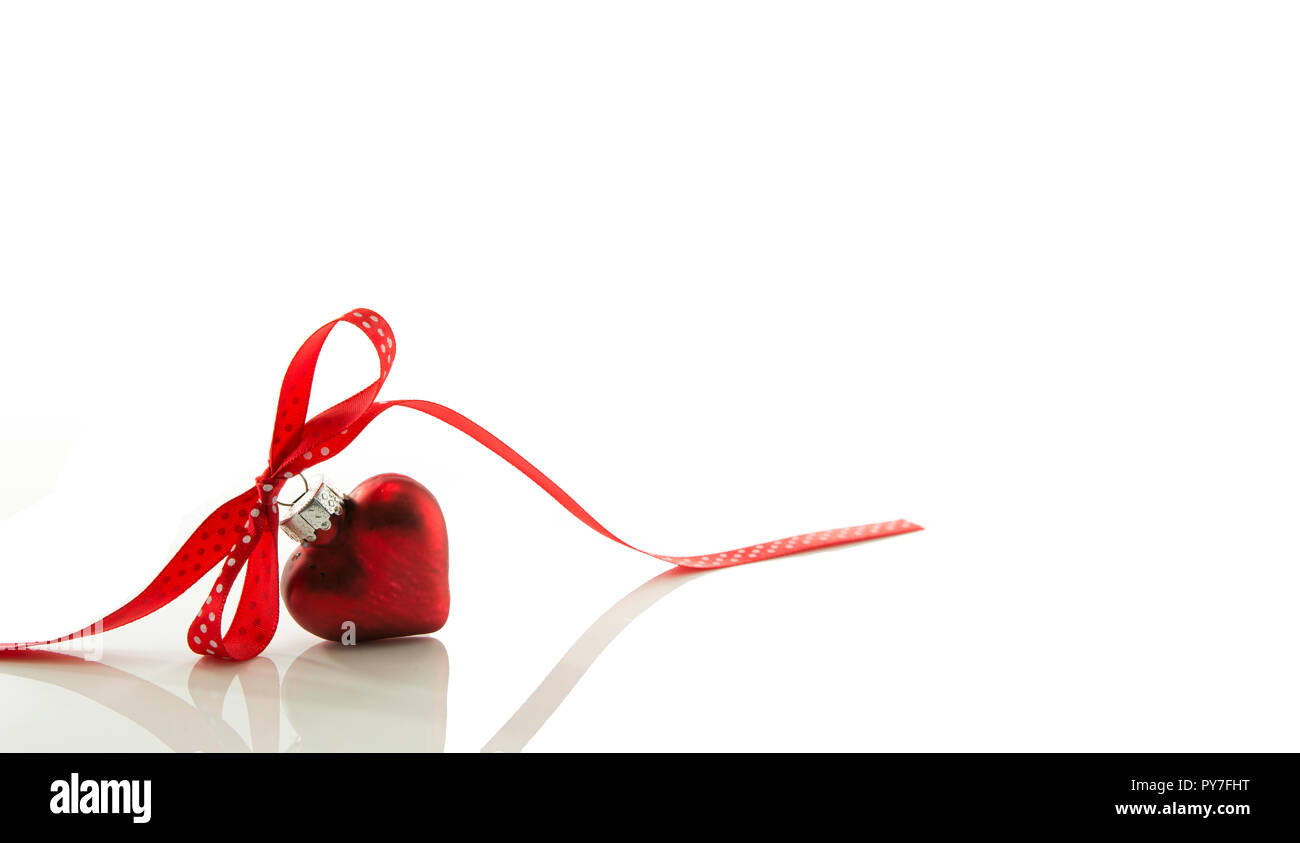 Corazón rojo para la Navidad con un arco de una cinta roja aislado sobre la cinta blanca Foto de stock