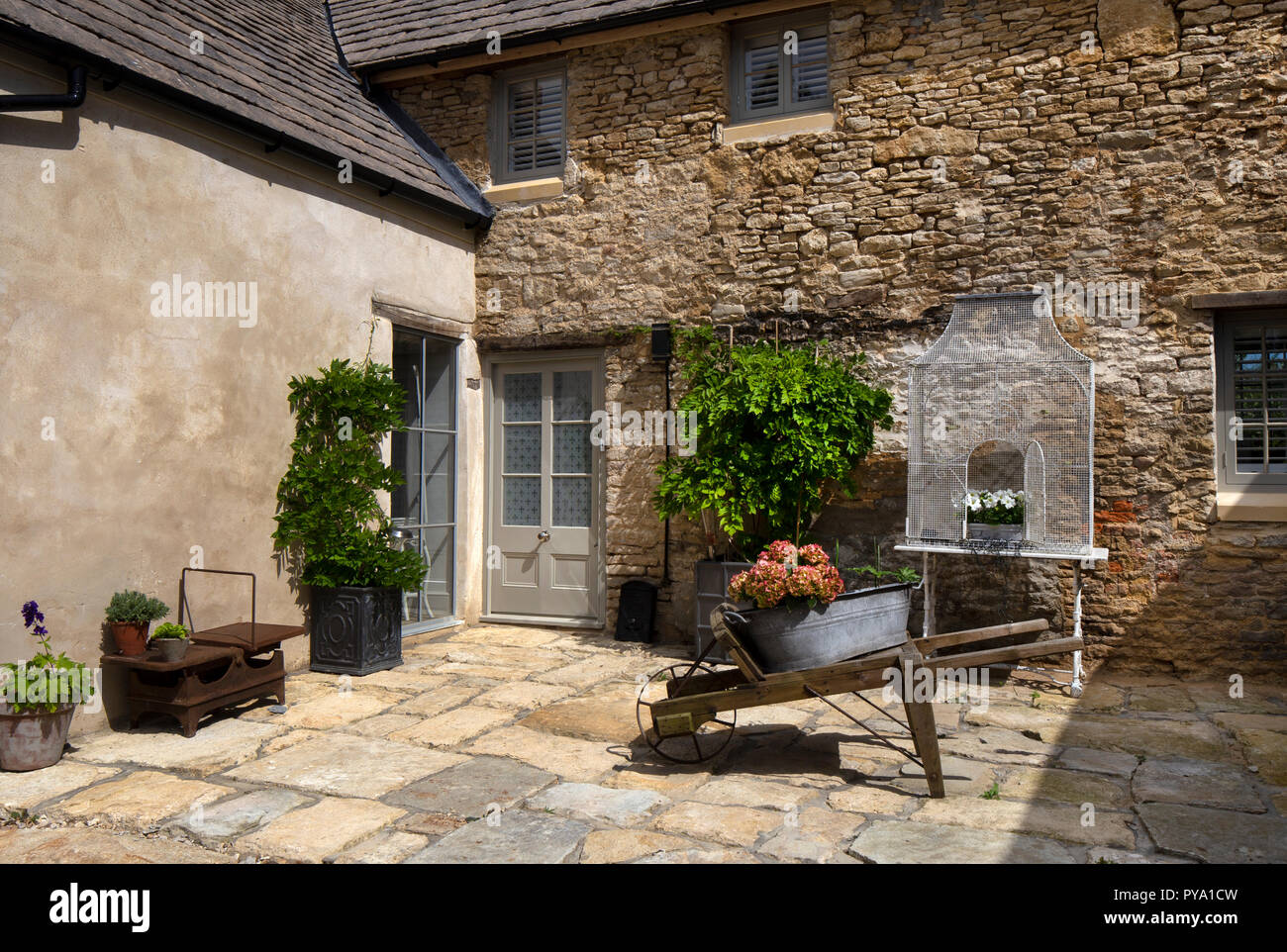 Carretilla de madera con hydrangea y wisteria en olla de metal fuera de casa en el patio de piedra en el Jardín Inglés,Inglaterra,Europa Foto de stock