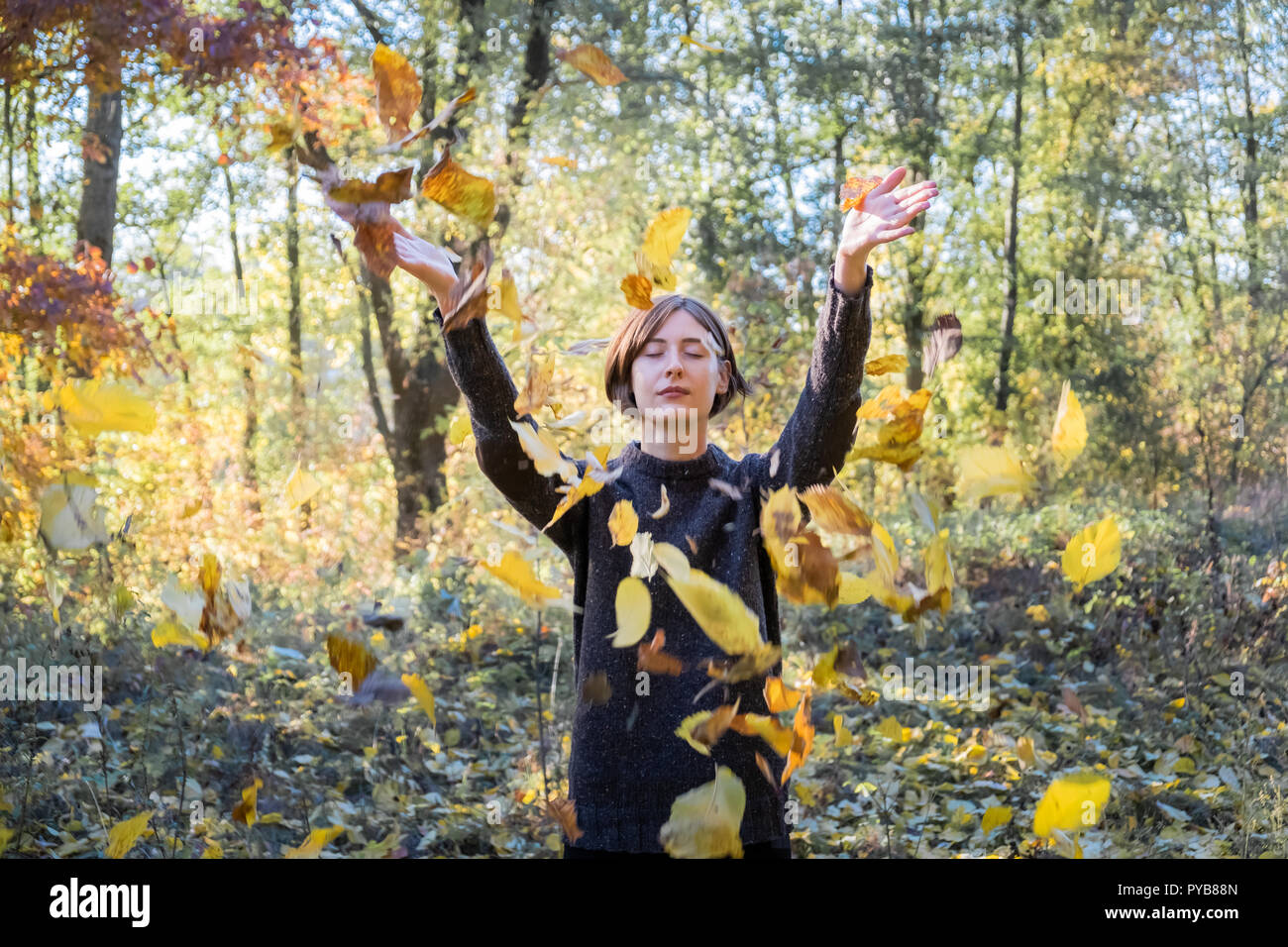 Mujer lanza otoño hojas amarillas en el aire. Retrato de mujer joven relajado con los ojos cerrados y coloridas hojas volando a su alrededor. Foto de stock