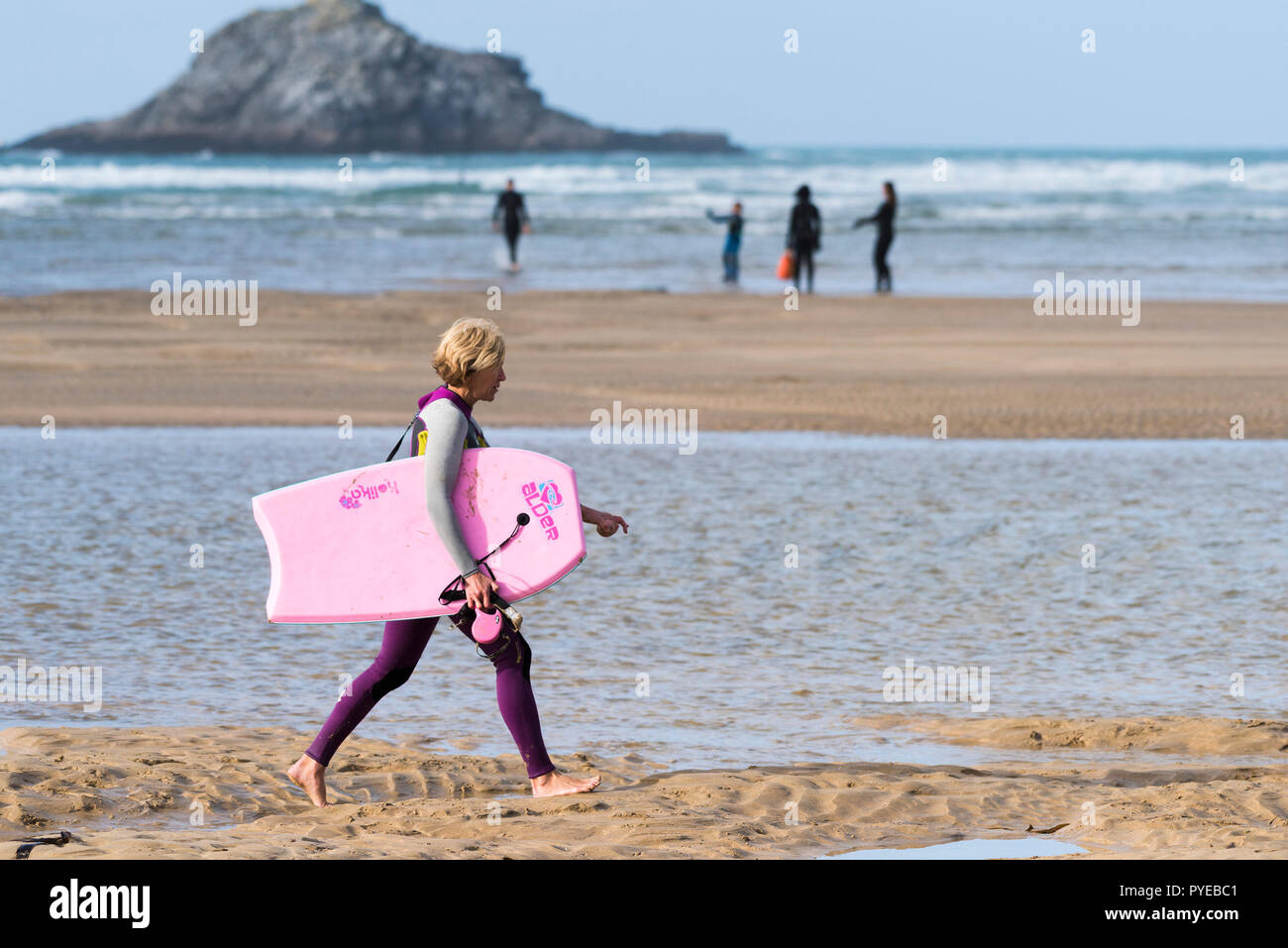 Playa Crantock en Newquay en Cornualles - una mujer madura vacacionistas en un traje de neopreno, llevando un cuerpo rosa boogie board caminando a lo largo de la costa. Foto de stock