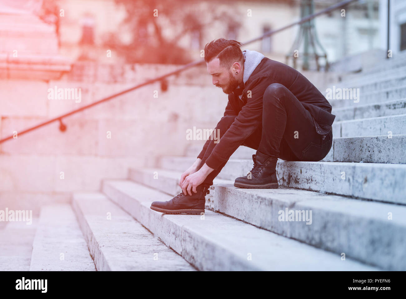 Estilo retro foto de un joven hipster hombre sentado en las escaleras y  atar sus zapatos Fotografía de stock - Alamy