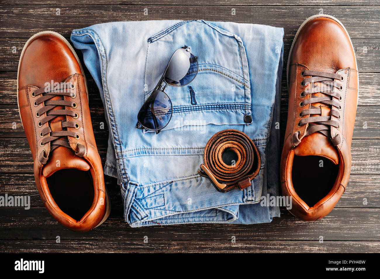 Hombre de botas de cuero marrón, cinturones, gafas de sol y pantalones vaqueros  azules sobre fondo de madera oscura, vista superior Fotografía de stock -  Alamy