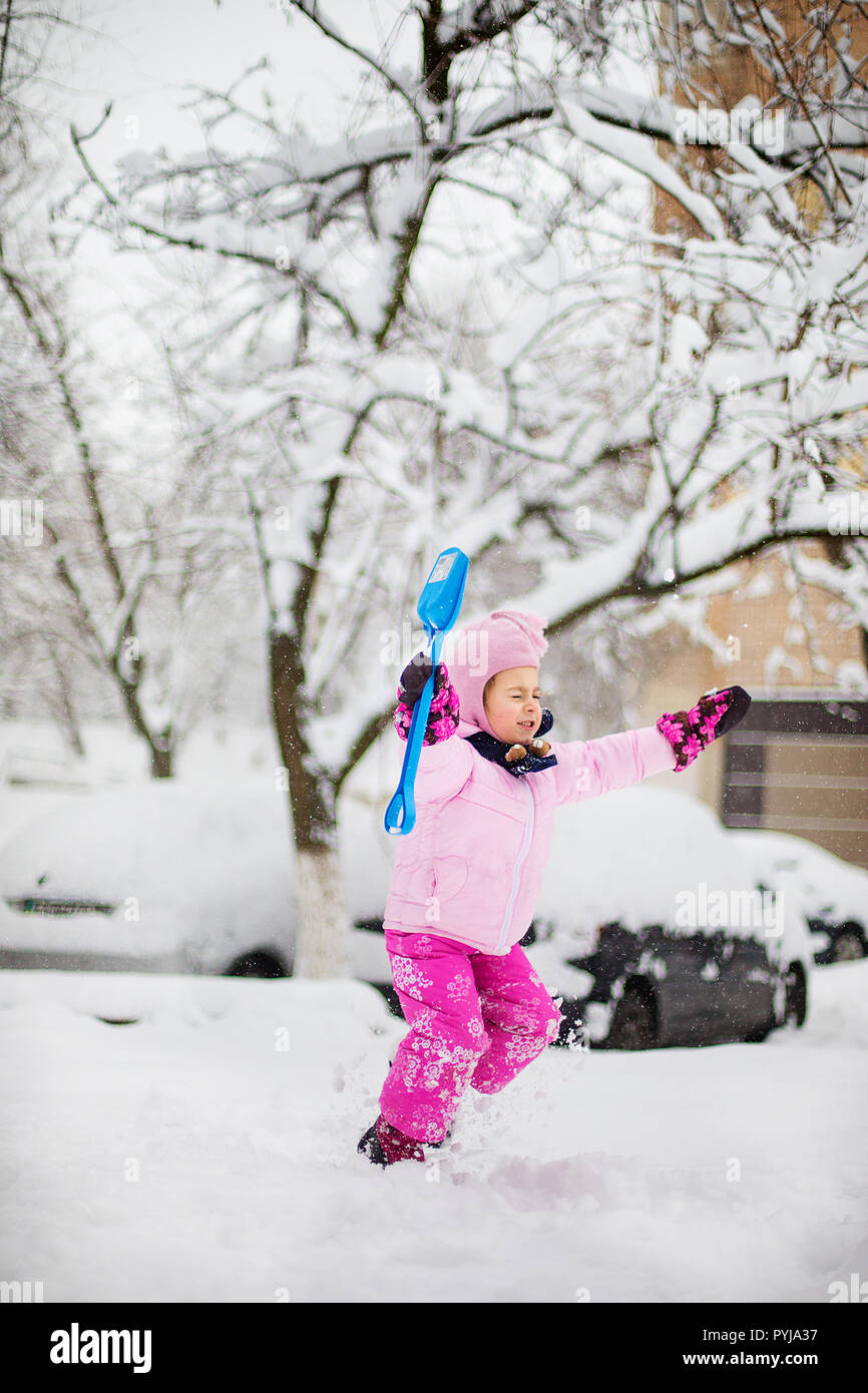 El niño juega con la nieve en el invierno. Una niña en una chaqueta y gorro  de punto brillante, atrapa a los copos de nieve en Winter Park para Navidad  Fotografía de