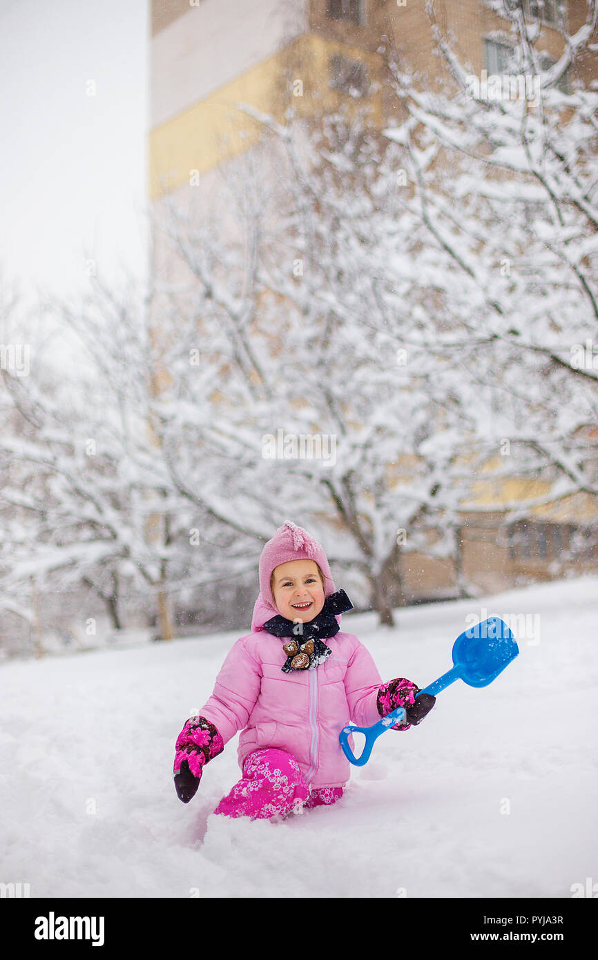El niño juega con la nieve en el invierno. Una niña en una chaqueta y gorro  de punto brillante, atrapa a los copos de nieve en Winter Park para Navidad  Fotografía de
