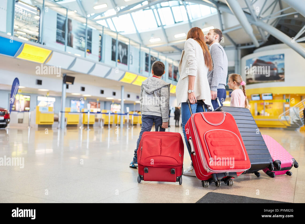 Familia Feliz y dos niños con el equipaje en la terminal del aeropuerto están a la espera de su salida Foto de stock