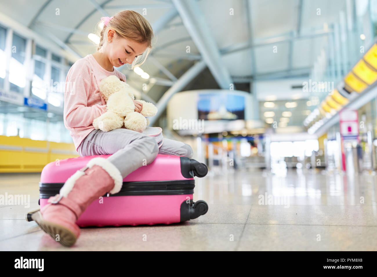 Niña está esperando en la terminal del aeropuerto para la partida y juega con un animal de peluche Foto de stock