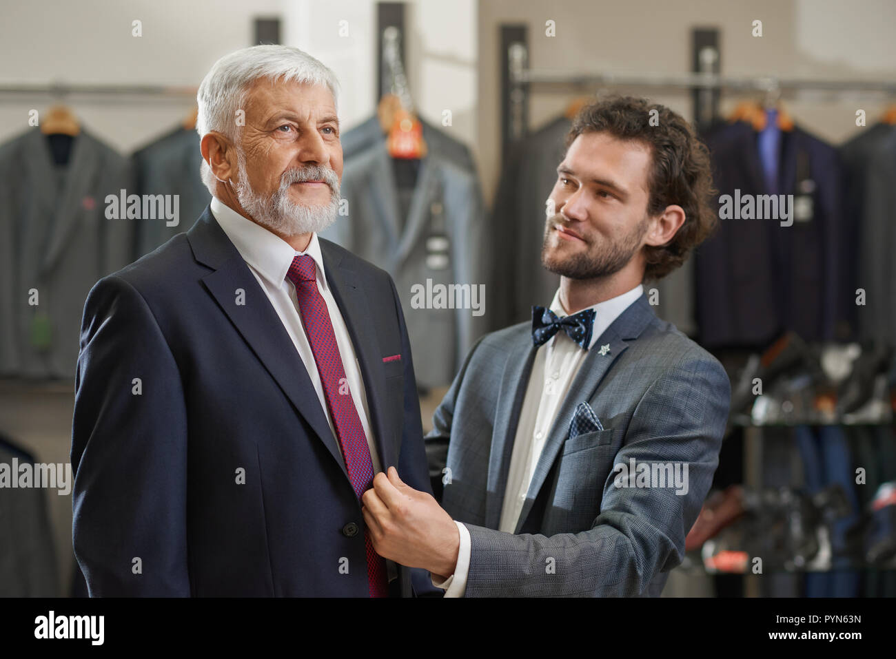 Cerca de dos elegantes hombres próximos a la boutique de moda en compras. Padre  e hijo buscando ropa para occaision especial. Los clientes en elegantes  trajes truing en Nueva colección en tienda