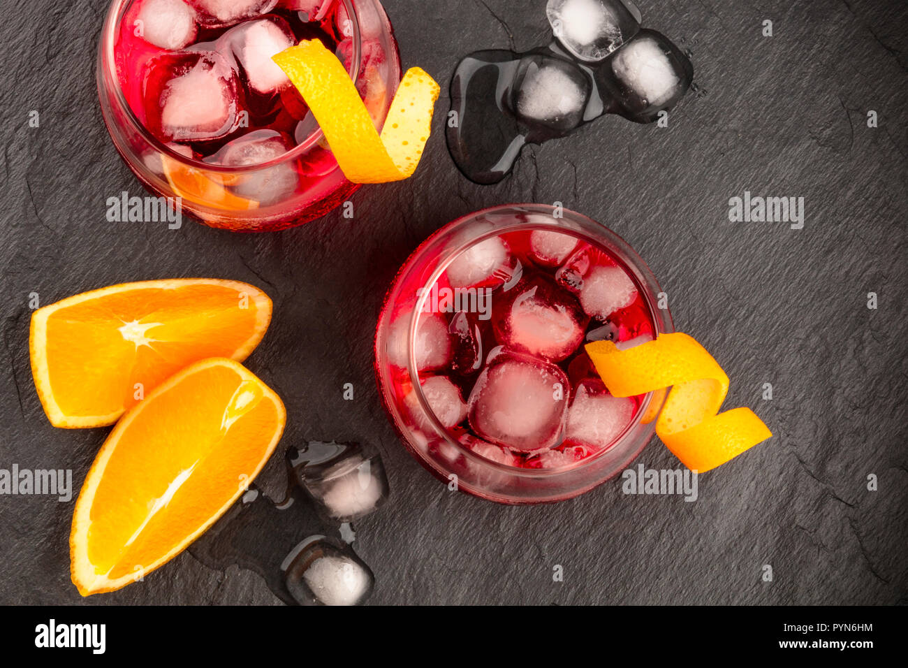 Dos vibrantes Negroni cócteles con campari y la ralladura de naranja trenzado aderezos, tomada desde la parte superior, con cubitos de hielo y rodajas de frutas sobre un fondo negro, con un lugar para el texto Foto de stock