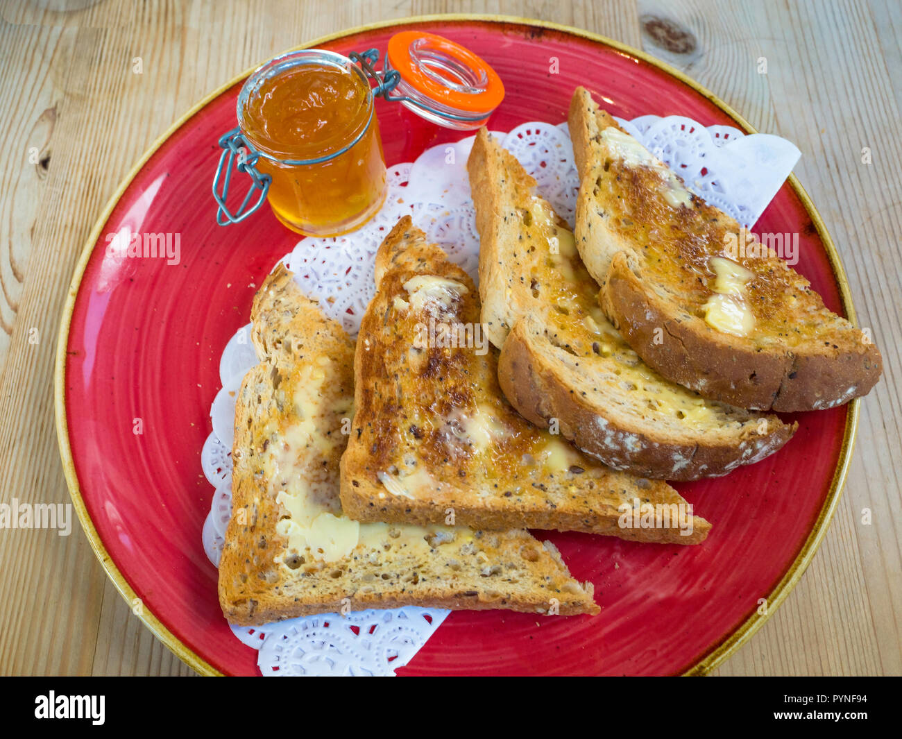 Pan tostado untado con mantequilla multigrain marrón y un tarro de mermelada, un desayuno, merienda o aperitivo en Inglaterra Foto de stock