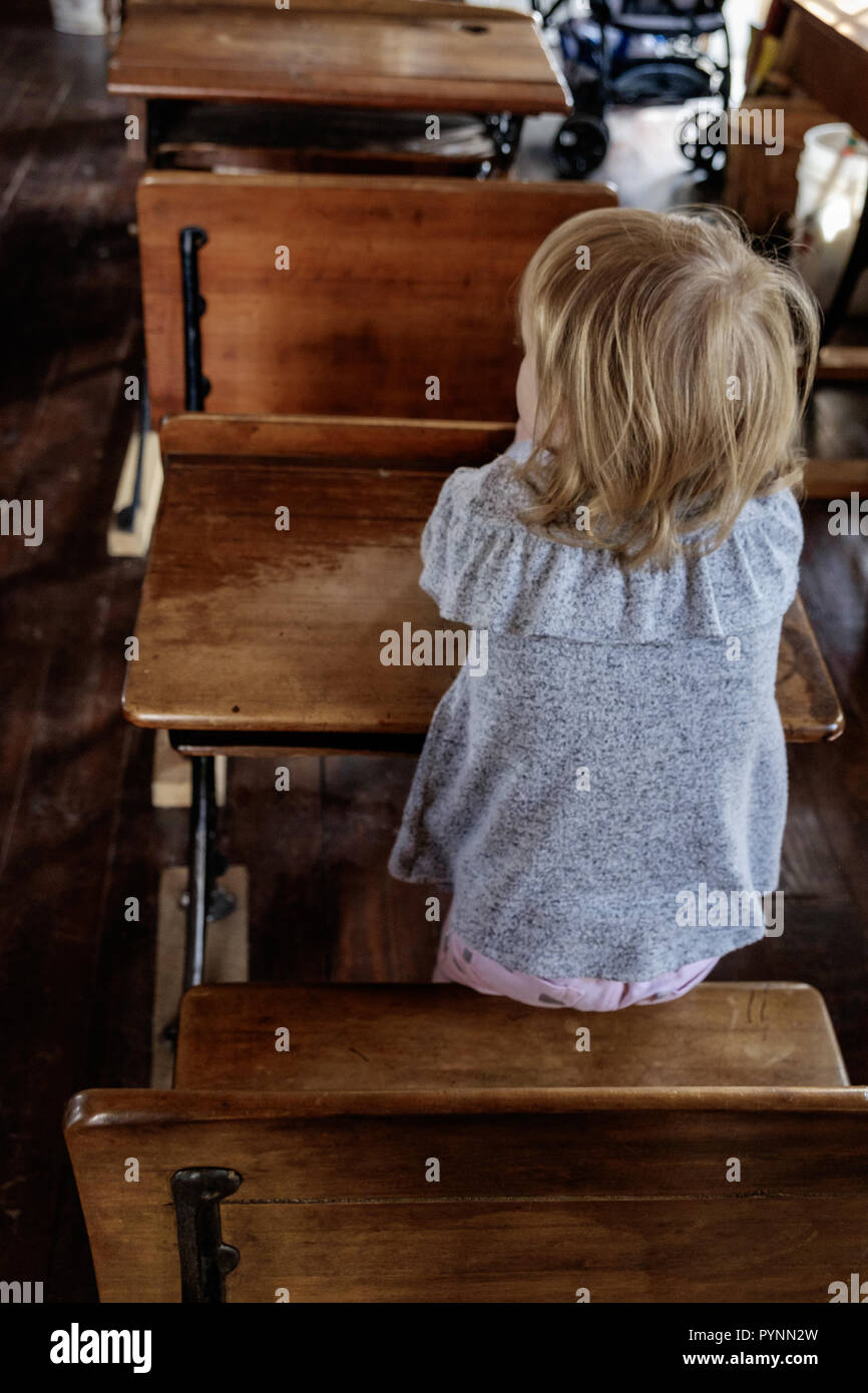 Niña de la escuela en un vestido vintage se asienta en un mostrador de madera en el aula. Wilmeth Schoolhouse, plaza de castaños Pueblo Histórico, McKinney Texas retrato. Foto de stock