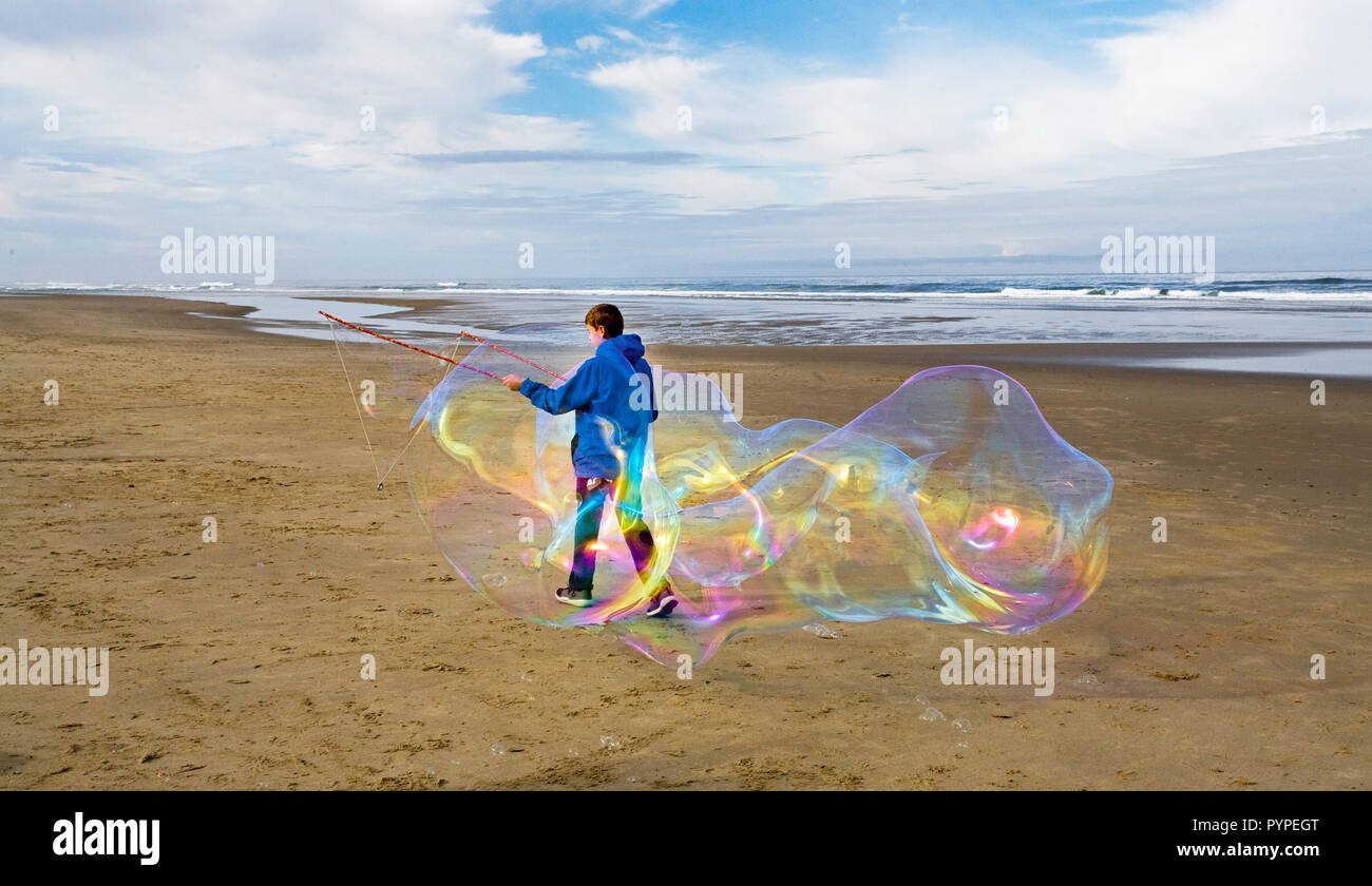 Un adolescente con una varita de burbuja crea una enorme burbuja de jabón en el Océano Pacífico, cerca de la ciudad de playa Yachats, Oregon. Foto de stock