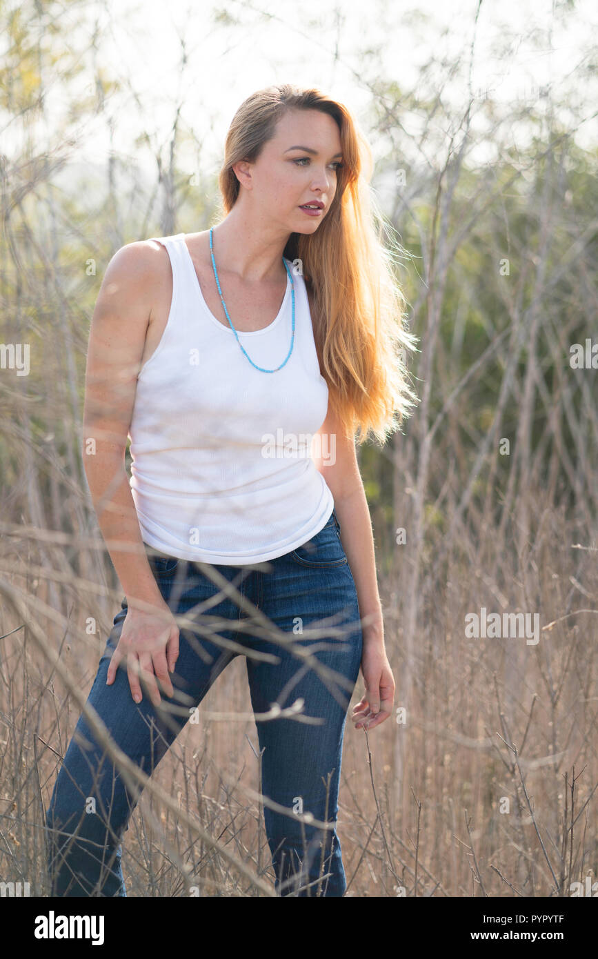Una joven mujer plantea en campo abierto, llevaba una camisa blanca y  pantalones de mezclilla Fotografía de stock - Alamy