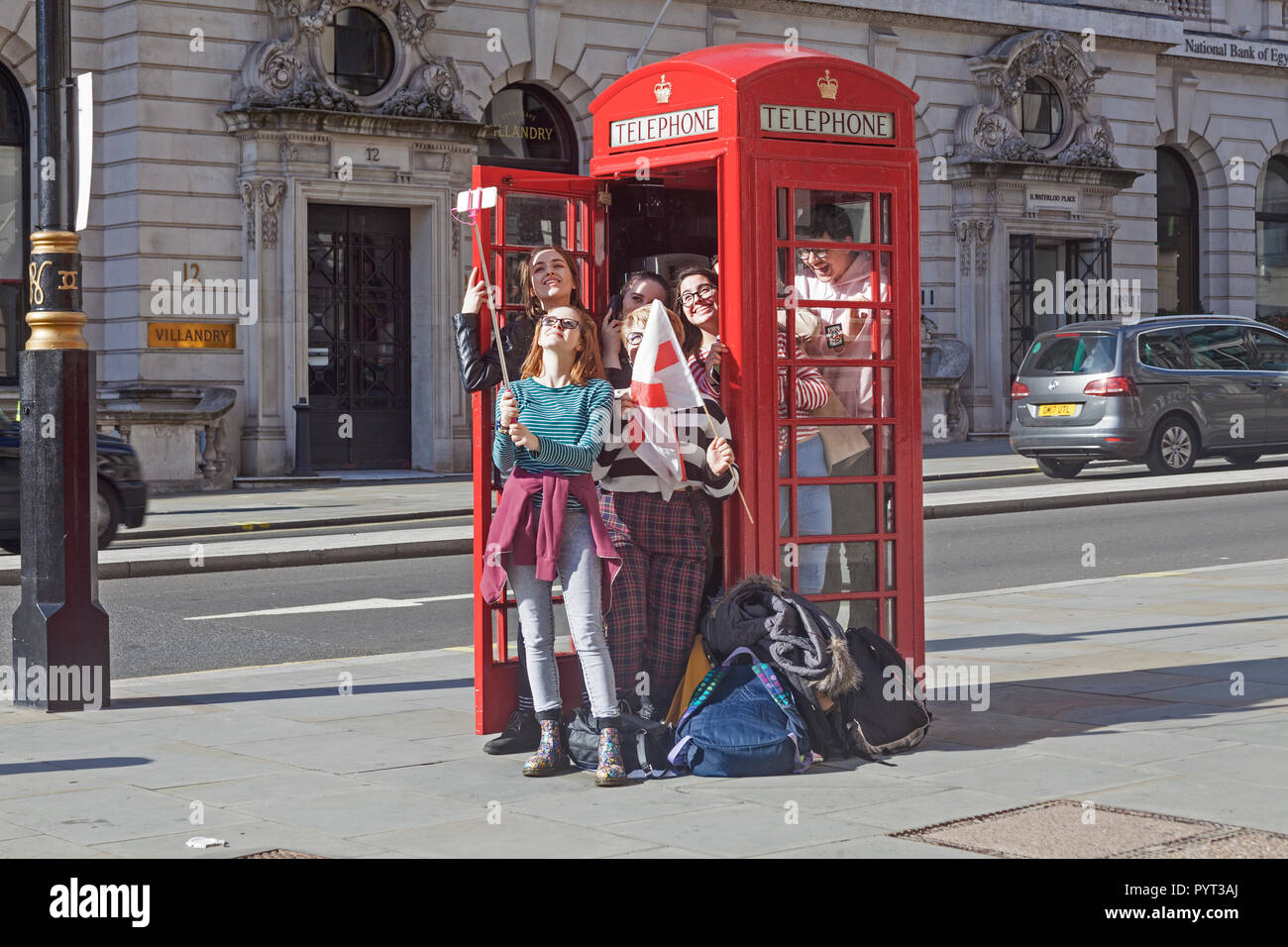 Una parte de las hembras jóvenes turistas tomando un selfie después de probar la capacidad de un teléfono rojo tradicional cuadro en Londres Waterloo Place. Foto de stock