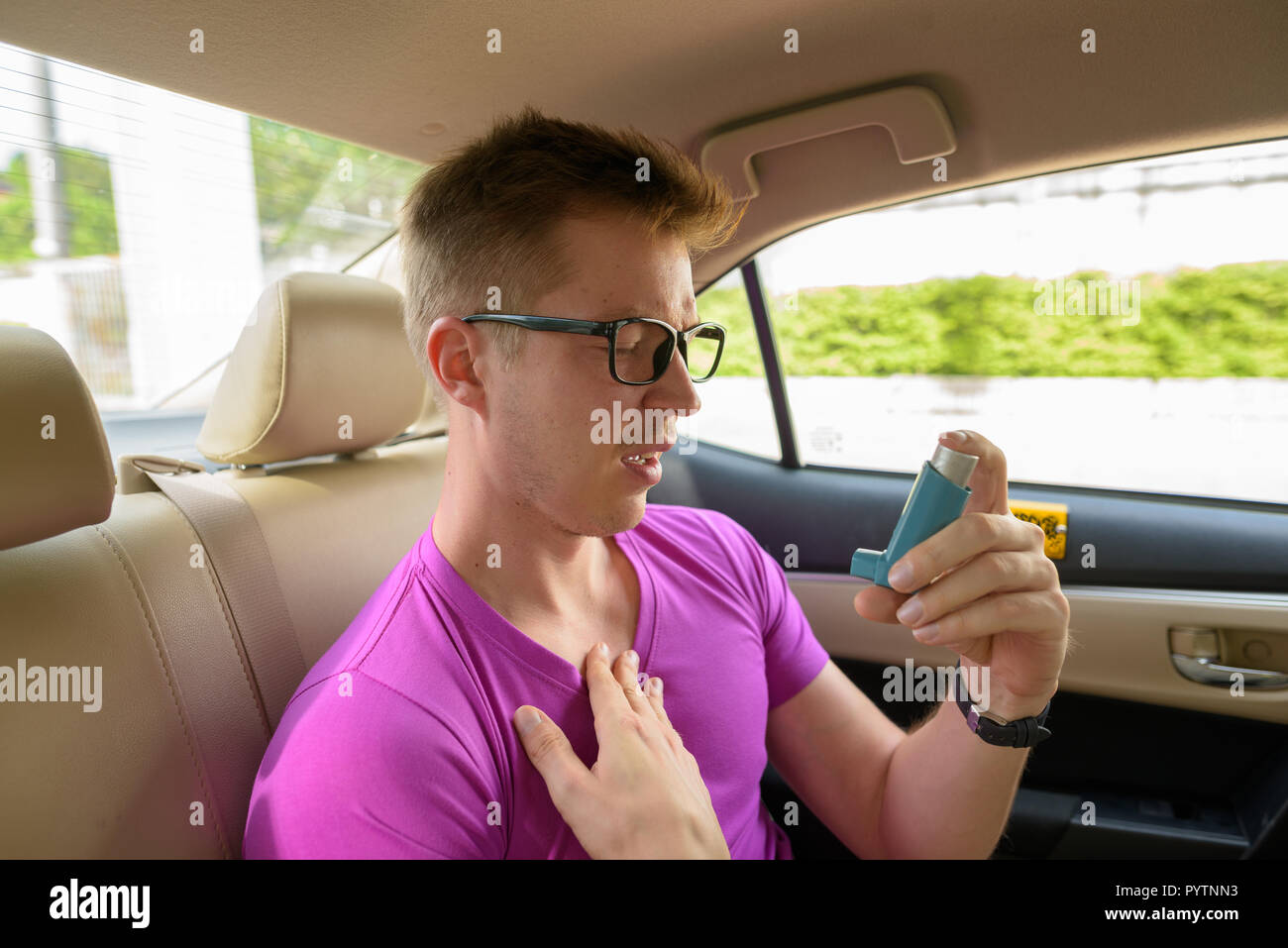 Hombre utilizando inhalador para el asma en el asiento de atrás del coche Foto de stock