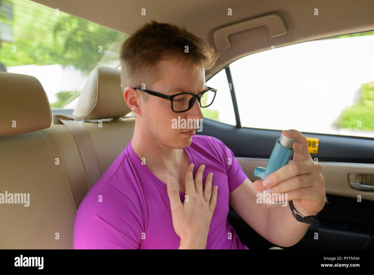 Hombre utilizando inhalador para el asma en el asiento de atrás del coche Foto de stock