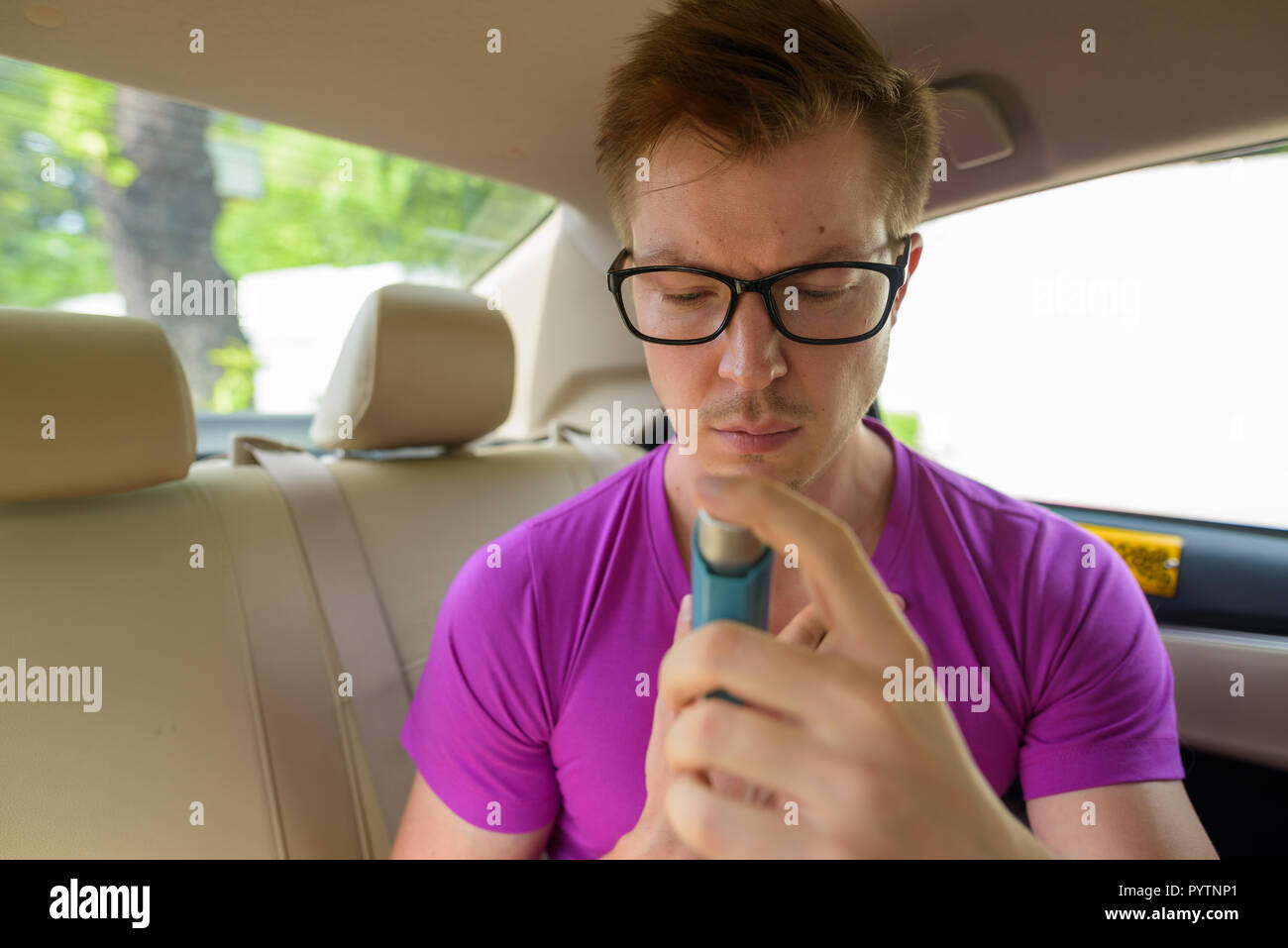 Rostro del hombre mediante inhalador para el asma en el asiento de atrás del coche Foto de stock